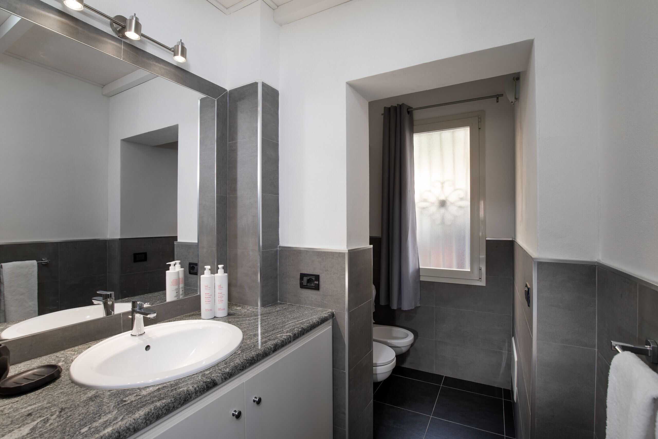 A modern bathroom with a granite countertop, a large mirror, and a shower area.