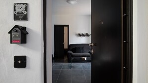 En modern inredning med en svart dörr, en svart soffa och ett litet bord med böcker. Det finns väggmonterade ljusströmbrytare och en skylt ovanför dörren.