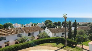 A coastal residential area with white buildings, a palm tree, and a clear view of the sea.