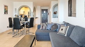 A modern living room with a grey sofa, black chairs, and a dining area with a table and chairs.