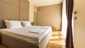 Moderni hotellihuone, jossa on suuri sänky, yöpöytä ja ikkunasta avautuva näkymä ulos.
