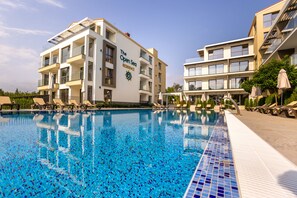 A swimming pool with lounge chairs and umbrellas, surrounded by multi-story buildings with balconies and a sign reading "The Open Sea Residence". - Open sea residence (Obzor)
