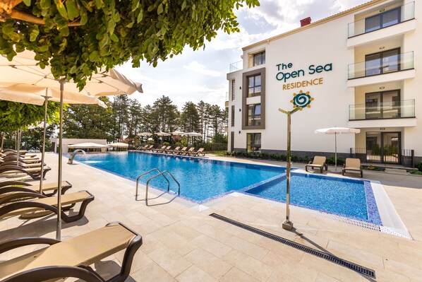 A swimming pool with lounge chairs and umbrellas, surrounded by a building labeled "The Open Sea Residence". - Open sea residence (Obzor)