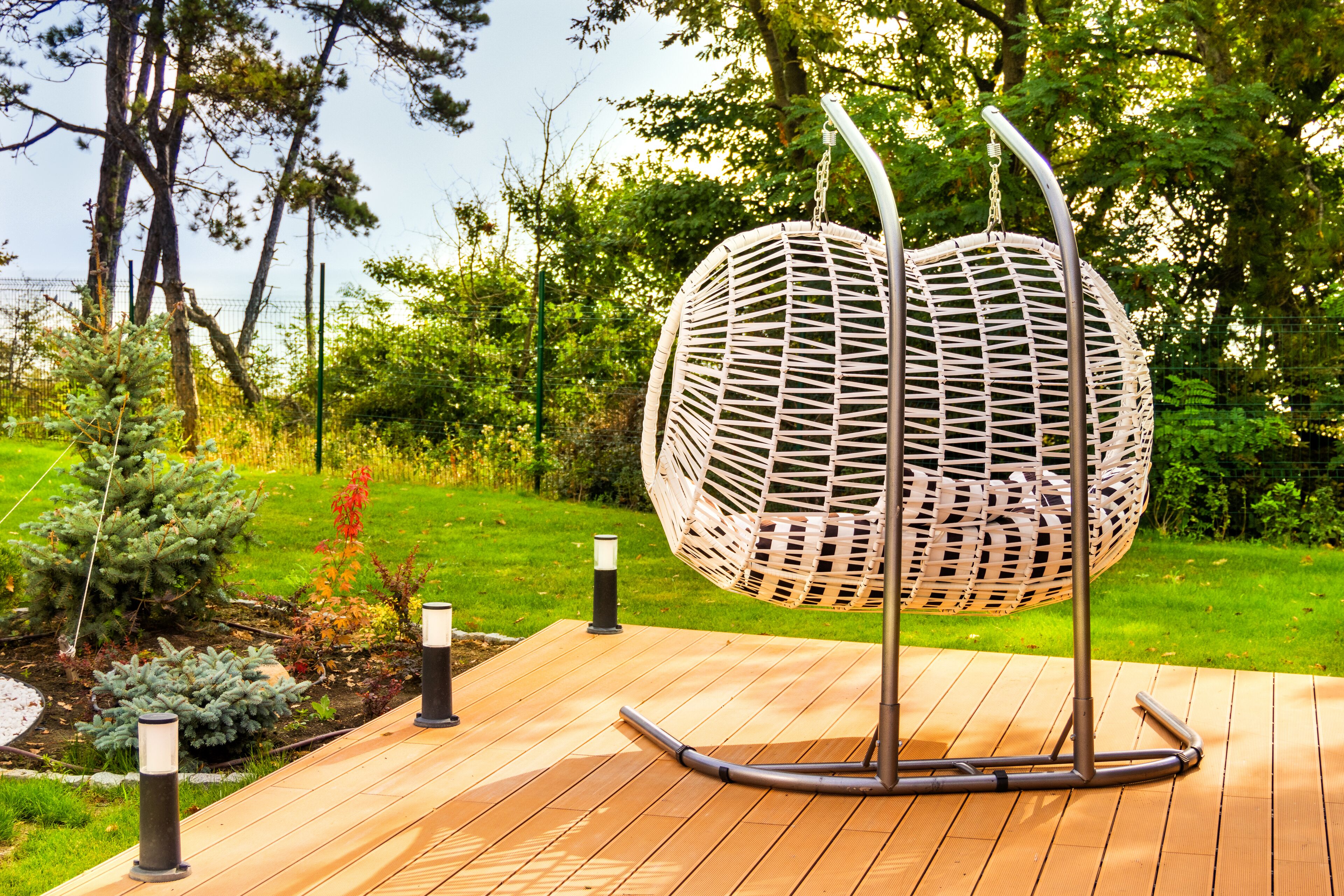 A wicker hanging chair on a wooden deck with a grassy garden and trees in the background.