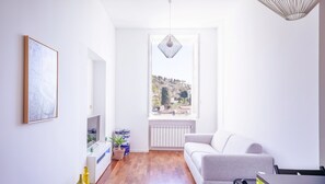 Un soggiorno moderno con un divano grigio, un tavolo da pranzo e vista su una collina.