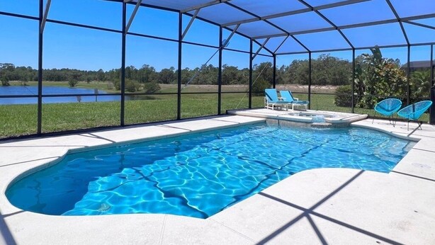 A covered swimming pool with a view of a lake and trees, surrounded by a metal frame and blue chairs. - Lakeside 5bd Pool Hm Spa Gm Watersng-237ys 5 Bedroom Home by RedAwning (Davenport)