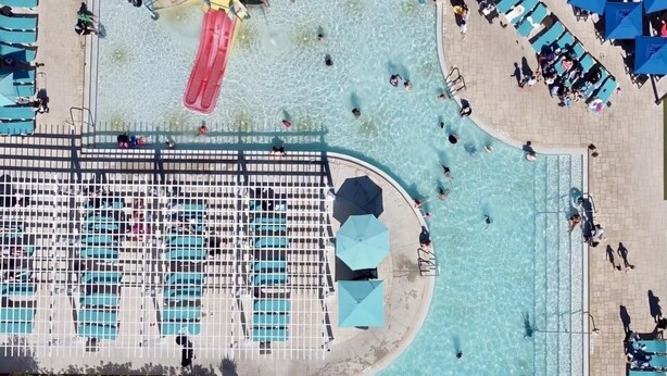 Vista aérea de una zona de piscina con varias piscinas, sillones de descanso y sombrillas.