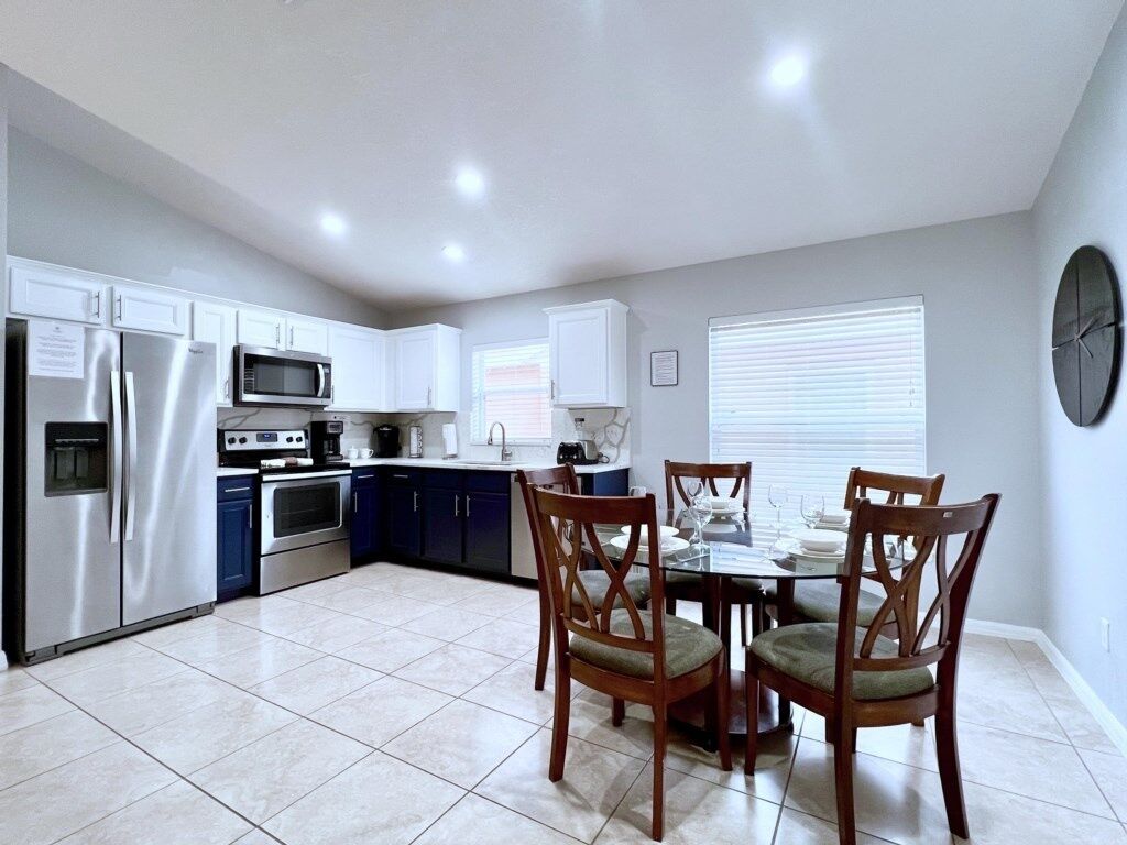 A modern kitchen with white cabinets, stainless steel appliances, and a dining area with a glass table and wooden chairs.
