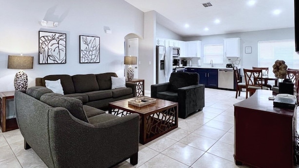 A modern living room with a sofa, armchairs, and a coffee table. There is a kitchen area with cabinets and a dining table. - Terrific Value 4bd Pool Gm Spa Hm Sandy Ridge-640b 4 Bedroom Home by RedAwning (Davenport)
