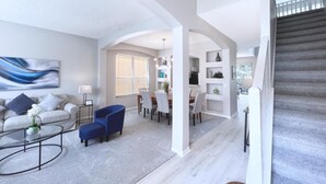 Un amplio salón con sofá, sillas y una mesa de centro. Una escalera conduce a un nivel superior.