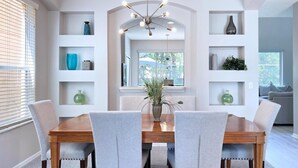 Un comedor con una mesa de madera y cuatro sillas, rodeado de estanterías blancas con objetos decorativos.
