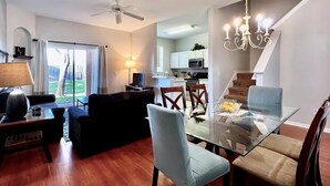 A modern living room with a glass dining table, comfortable seating, a ceiling fan, and a view of the kitchen and outdoor area. - Spacious 4bd Th Regal Palms 2530ca 4 Bedroom Townhouse by RedAwning (Davenport)