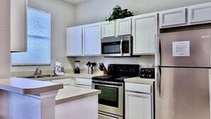 A modern kitchen with white cabinets, stainless steel appliances, and a central island. - Spacious 4bd Th Regal Palms 2530ca 4 Bedroom Townhouse by RedAwning (Davenport)