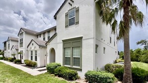 A row of two-story houses with a uniform architectural style, featuring a central entrance with a covered porch, and surrounded by well-maintained lawns and palm trees. - Colorful & Kid Friendly 5bd Pool Th Festival-422cd 5 Bedroom Townhouse by RedAwning (Davenport)