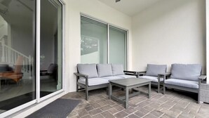 A patio with two grey sofas, a small table, and a sliding glass door. - Colorful & Kid Friendly 5bd Pool Th Festival-422cd 5 Bedroom Townhouse by RedAwning (Davenport)