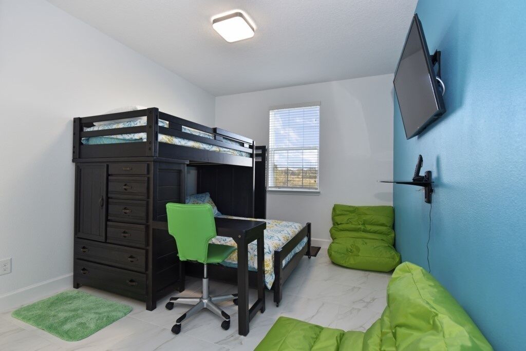A bedroom with a bunk bed, desk, chair, and green bean bag chairs.