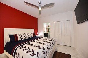 A bedroom with a bed, white walls, a red accent wall, a ceiling fan, and a TV mounted on the wall. - Colorful & Kid Friendly 5bd Pool Th Festival-422cd 5 Bedroom Townhouse by RedAwning (Davenport)
