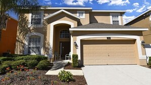 A two-story house with a beige exterior, a garage, and a well-maintained front yard with shrubs and flowers. - Watersong Resort 6bd Pool Hm,2 Master Suites-956oc 6 Bedroom Home by RedAwning (Davenport)