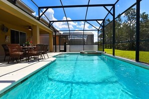 A swimming pool with a glass enclosure, surrounded by a patio with wicker furniture and a covered area. - Watersong Resort 6bd Pool Hm,2 Master Suites-956oc 6 Bedroom Home by RedAwning (Davenport)