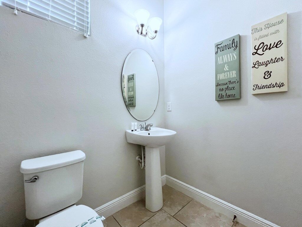 A bathroom with a toilet, sink, and mirror. There are two wall decorations with text.
