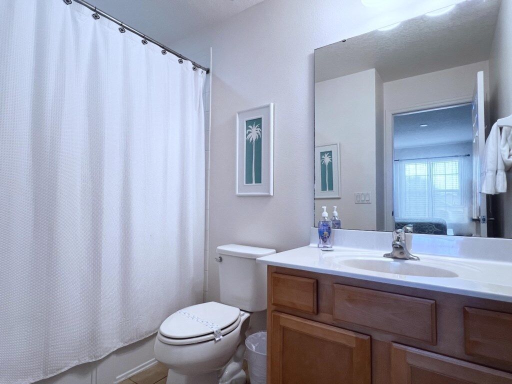 Un baño con inodoro, lavabo con espejo y cortina de ducha.