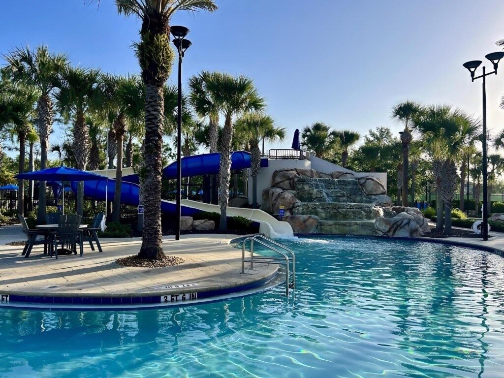 A pool area with a water slide, palm trees, and outdoor seating.