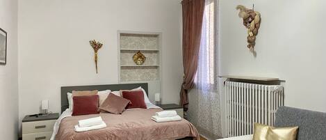 A bedroom with a bed, bedside tables, a chair, a radiator, and decorative wall art.