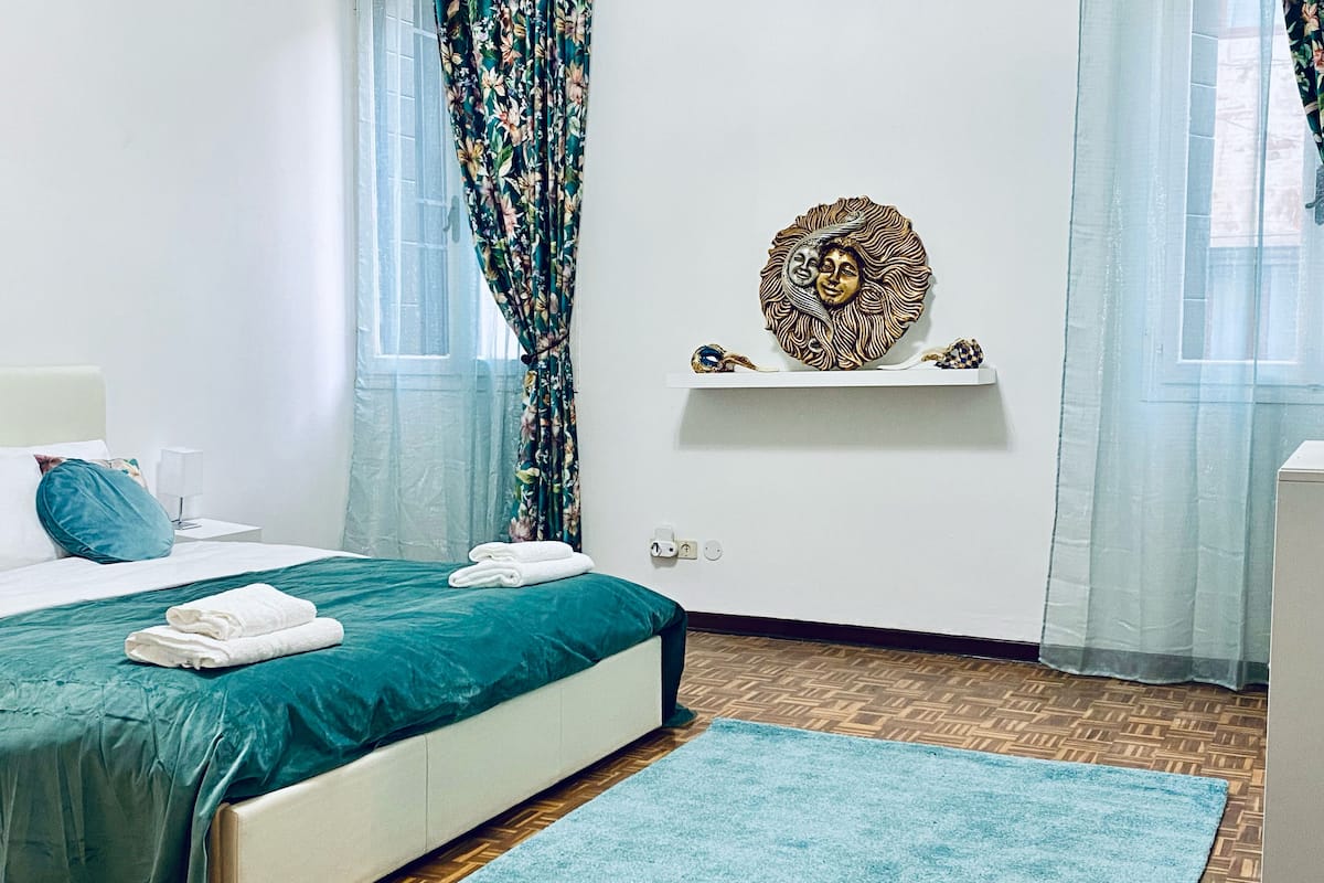 A neatly arranged bedroom with a bed, a small shelf with decorative items, and a patterned rug.