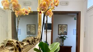 A hallway with a wooden reception desk, a white vase with green foliage, and a large ornate mirror reflecting the room. - La Dogaressa Guest House (Venice)