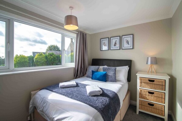 A neatly made bed with a blue and white duvet, a bedside lamp, and a window with curtains.