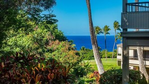 A view of a lush garden with palm trees and a building with a balcony overlooking the ocean. - Wailea Ekolu 1603 2 Bedroom Condo (Kihei)