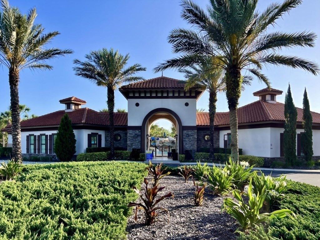 A building with a central archway, surrounded by palm trees and a well-maintained garden.