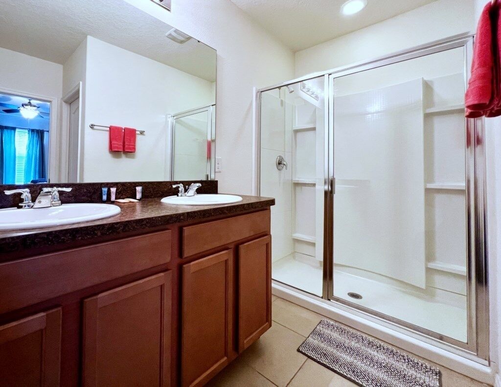 A bathroom with two sinks, a glass shower enclosure, and a red towel hanging on the wall.