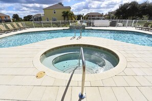 Ein Swimmingpool mit einem Whirlpool in der Mitte, umgeben von Liegestühlen und einem Zaun.