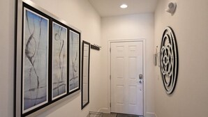 A hallway with framed abstract art, a white door, and a wall-mounted decorative piece. - Beautiful 3-bed Villa 10 Minutes From Disney-17440 Serenity Resort 3 Bedroom Townhouse by RedAwning (Clermont)