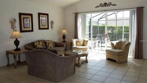 A living room with a sofa, two armchairs, a coffee table, and a glass-top table. There are two lamps on side tables, and a large window with a view of greenery outside. - Lovely 4bd Gm Spa Pool Hm Glenbrook-1616msd 4 Bedroom Villa by RedAwning (Clermont)