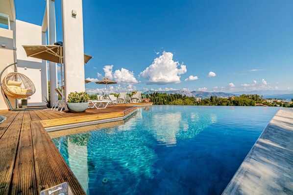 Relax by the serene infinity pool surrounded by a wooden deck and lush greenery.
