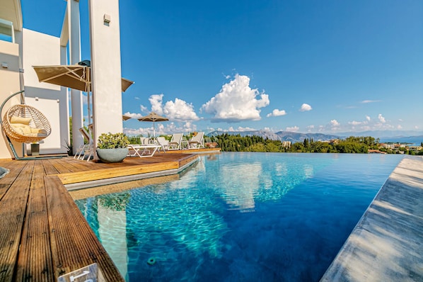 Relax by the serene infinity pool surrounded by a wooden deck and lush greenery.
