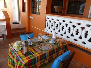 Un coin repas avec une table dressée pour deux personnes, agrémentée d’une nappe à carreaux colorés, d’un pichet en métal, d’un verre contenant un objet décoratif et d’une assiette avec une fourchette et un couteau.
