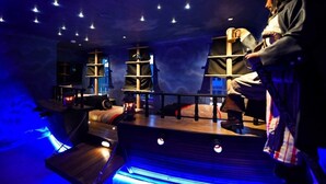A room with a wooden ship-themed decor, including a ship-shaped bookshelf and a ship's wheel.