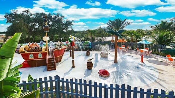 A water park with a ship-themed play area, a water slide, and a fenced seating area.