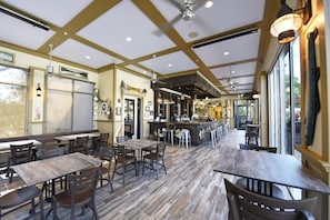 Un ristorante con un'area bar, tavoli e sedie in legno e ampie finestre.