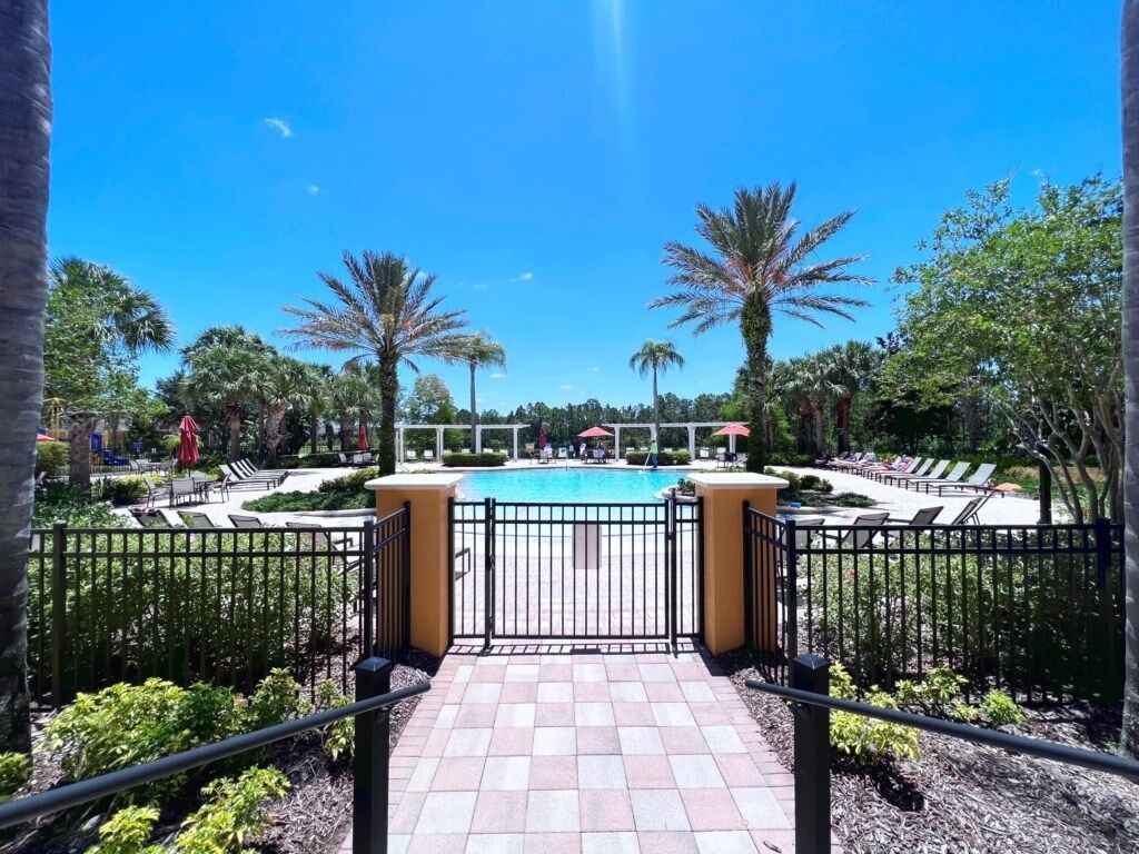 A pool area with a tiled walkway, palm trees, and lounge chairs.