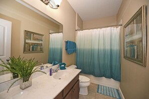 A bathroom with a double sink vanity, a toilet, a shower with a blue curtain, and a framed picture on the wall. - Meticulous 6bd Spa Gm Pool Hm Solterra-4187od 6 Bedroom Home by RedAwning (Davenport)