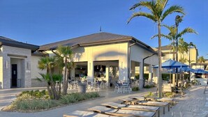 A hotel with outdoor seating, palm trees, and a pool area.