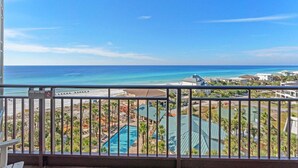 Un balcón con vistas a una playa, una piscina y edificios de un complejo turístico.
