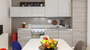 A modern kitchen with white cabinetry, a dining table with a fruit bowl, and a red trash bin. - notaMI - CASA RELAX - Central Station (Milan)