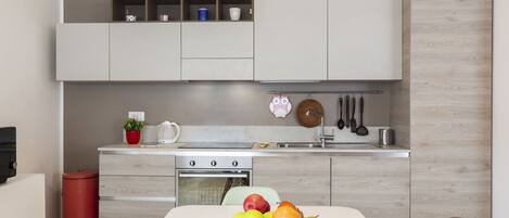 A modern kitchen with white cabinetry, a dining table with a fruit bowl, and a red trash bin.