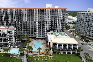 A high-rise hotel with multiple balconies, a rooftop pool, and a well-maintained lawn area.