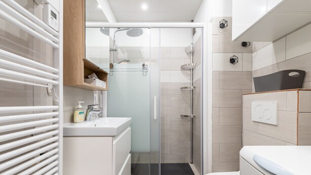 Een moderne badkamer met een douchecabine van glas, een witte wastafel en een toilet.